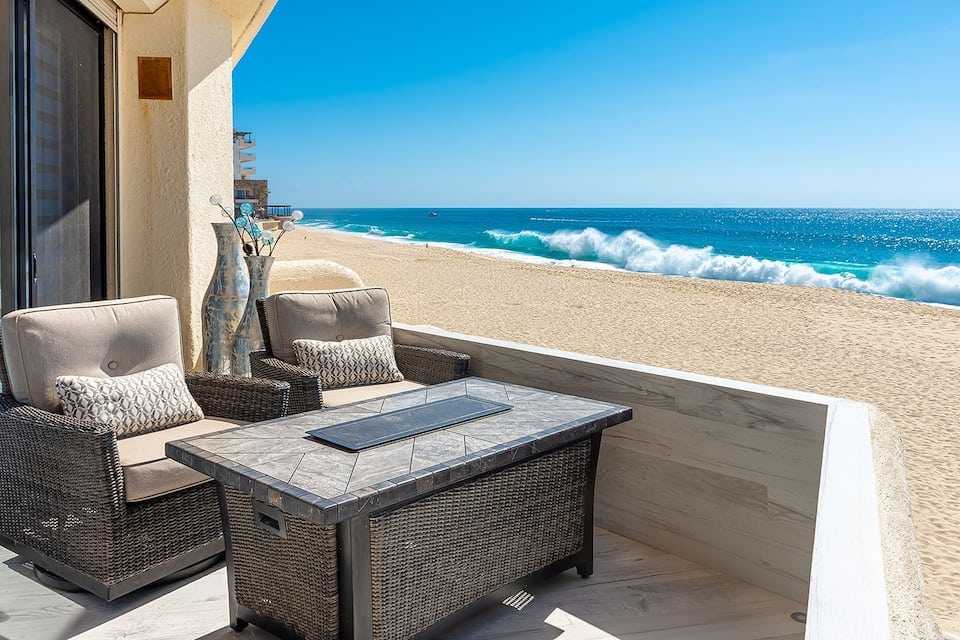 the private patio of a condo. The beach is immediately outside and the water is very blue and the wave are crashing on the sand.