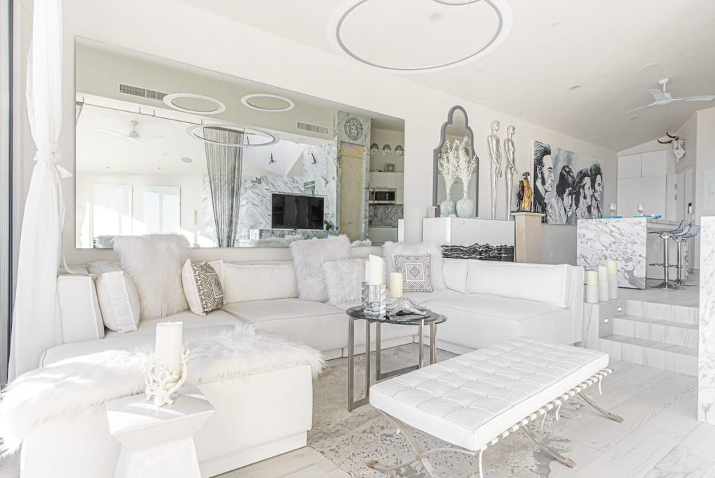 The interior of a sleek and modern condo. Everything in the condo is white including the furniture, walls, and flooring. It looks very plush.
