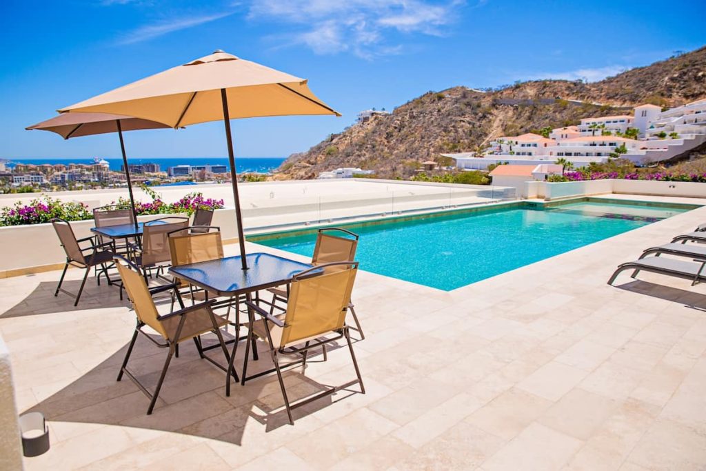 rooftop pool of the Vista Del Mar. There is pool as well as tables and chairs and umbrellas. There is a lovely view with the ocean in the background.